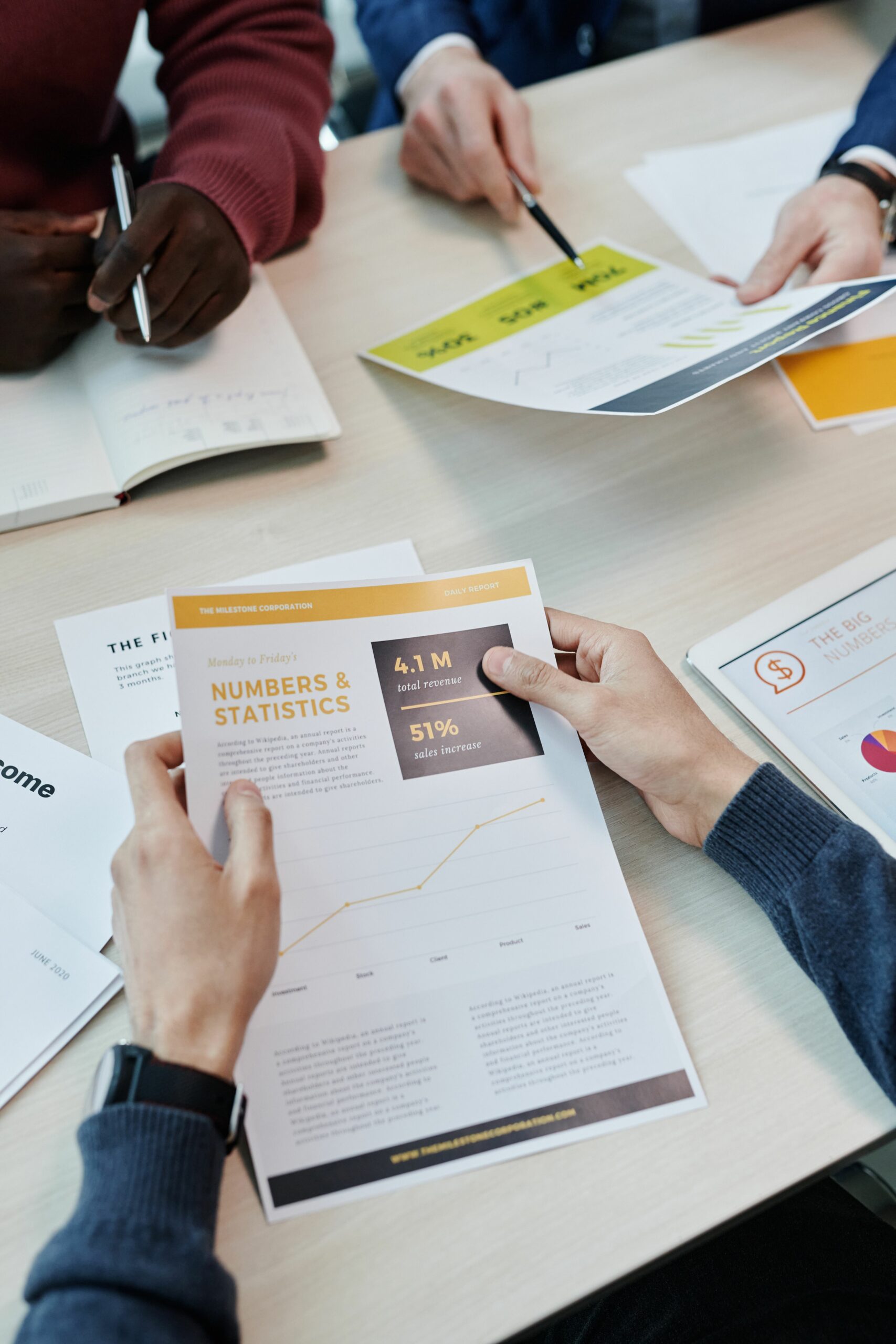 A group reviews business statistics and reports on a wooden table.