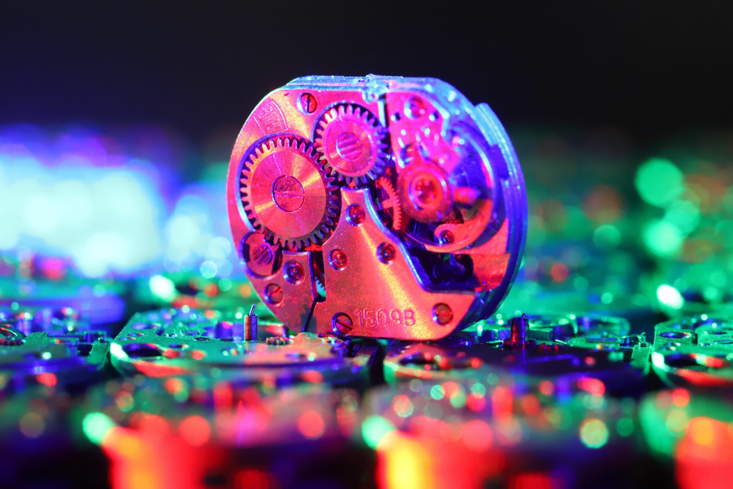 Metal watch movement with wheels placed on stack of stainless wrist watch parts in dark room on blurred background with bokeh
